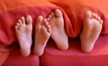 Nackte Füße schauen aus der Bettdecke